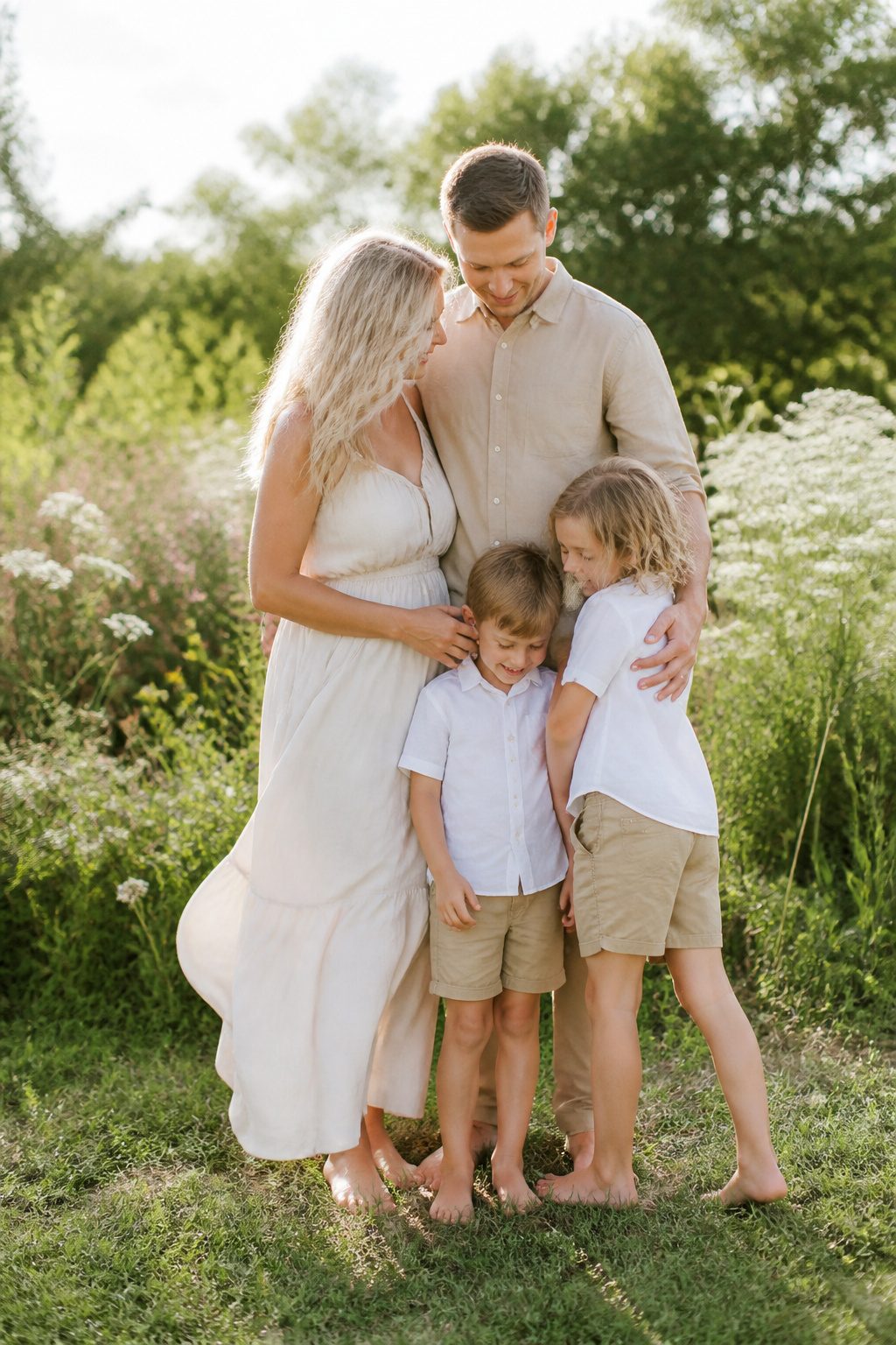 Family in cream, tan, and soft white outfits on green grass.