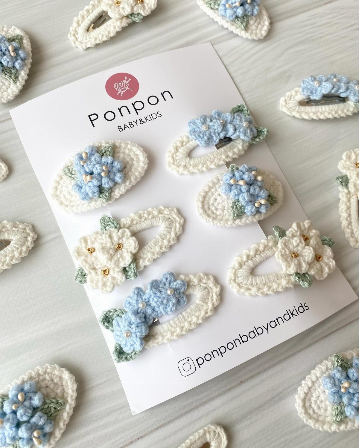 Handmade crochet hair clips with blue and white flowers scattered on a white surface.