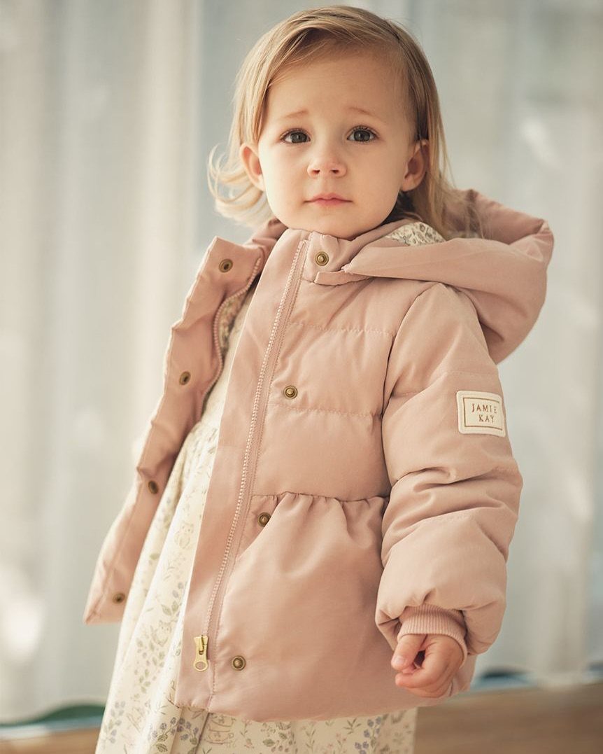 Toddler girl wearing a dusty pink hooded puffer jacket and a floral dress.