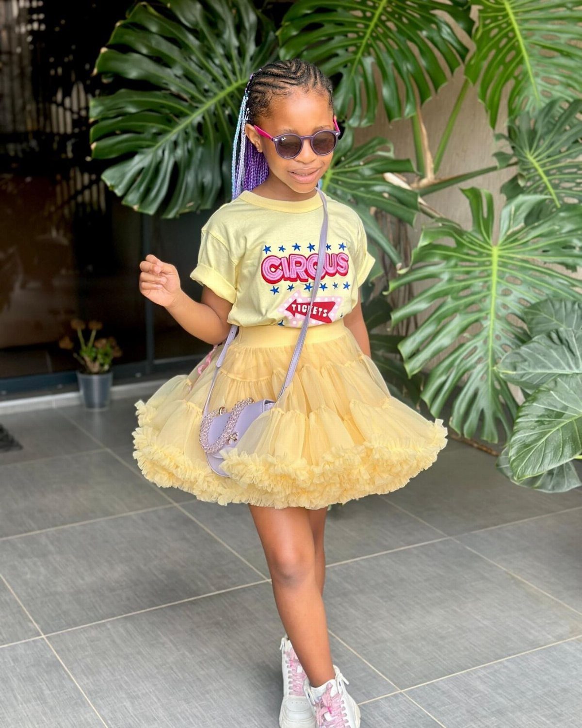 A young girl wearing a yellow graphic tee and a fluffy yellow tutu skirt.